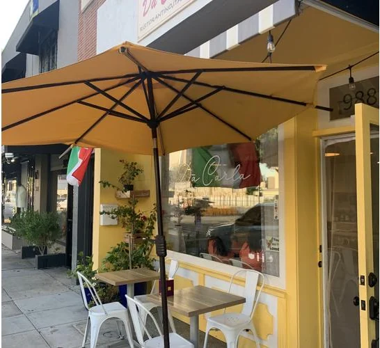 The Da Carla storefront on Santa Monica Boulevard: yellow facade, Italian flag and tables under a yellow umbrella
